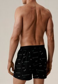 Czarne bokserki z motywem związanym z grami, z zielonymi napisami i ilustracjami ciężarów oraz symboli gier. Elastyczny pas.