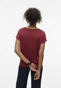 Top burdeos de manga corta con un corte relajado, textura suave y puños enrollados. Combinado con jeans de mezclilla oscuros, presentando un diseño sencillo y casual.