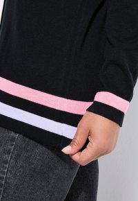 Schwarzer Strickpullover mit pink-weißen Streifen am Saum und an den Bündchen. Weiche Textur mit tailliertem Schnitt und ellbogenlangen Ärmeln.