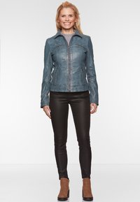 Blauwe leren jas met stiksels en ritszakken, getailleerd ontwerp, gedragen over zwarte slim-fit jeans en bruine enkellaarsjes.