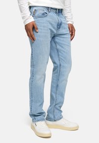 Vaqueros de denim azul claro con un diseño de pierna recta, que presentan sutiles patrones de desgaste y detalles de costura, combinados con deportivas blancas.