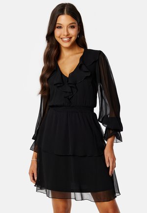 Schwarzes Kleid mit geschichteten Rüschen, langen transparenten Ärmeln, einem V-Ausschnitt und elastischem Taillenbund. Weicher, leichter Stoff mit fließender Silhouette.