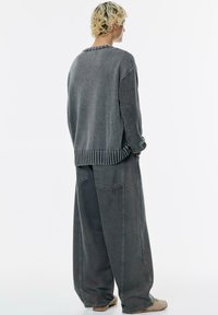Przesadny szary sweter z prążkowanym dołem i rękawami, zestawiony z luźnymi szarymi dżinsami. Stylizacja charakteryzuje się minimalistycznym designem i miękką fakturą.
