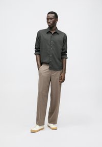 Chemise boutonnée charbon avec une texture subtile, associée à un pantalon beige à jambe droite et des baskets blanches. Design simple et moderne.