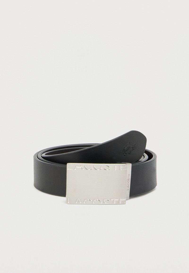 Ceinture en cuir noir avec une boucle rectangulaire en argent embossée du mot « LACOSTE ». La boucle présente une finition texturée et un petit détail de logo.