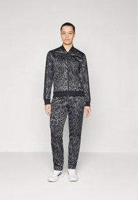 Svart atletisk treningsdress med jakke og bukse, begge med et teksturert dyreprintdesign og elastiske mansjetter, kombinert med hvite joggesko.