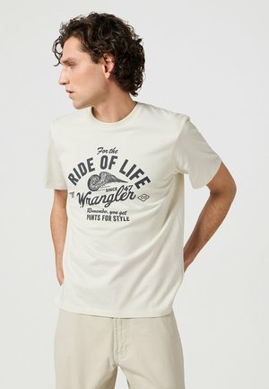 Cream short-sleeve t-shirt featuring a graphic print in black reading "Ride of Life" and "Wrangler." Smooth texture, standard fit, casual design.