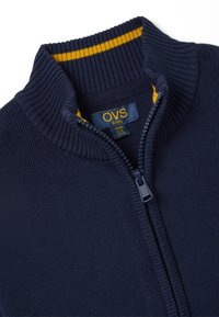 Marineblauer Kuschelpullover für Kinder mit einem gerippten Kragen und gelben Streifenelementen. Weicher Stoff mit glatter Textur und hochwertigem Reißverschluss.