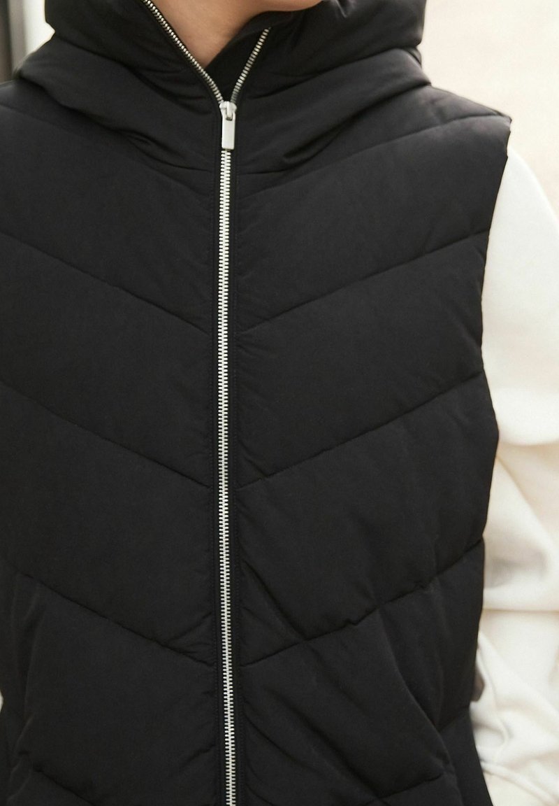 Czarna pikowana kamizelka z kapturem, z przeszywanym wzorem, zapinana na zamek z przodu i z bocznymi kieszeniami. Gładka tekstura i lekki materiał.