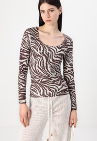 Pikad varrukad pruunis ja beežis zebra mustris top, mis on valmistatud pehmest kangast ja millel on ümar kaelus, kombineeritud tekstuursete valgete võrkpükstega.