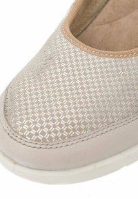 Zapato slip-on de color beige claro con un patrón texturizado de diamantes plateados, un forro interior suave y una suela de goma blanca.