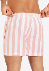 Rosa und weiße gestreifte Badehosen mit einem elastischen Bund und seitlichen Taschen, aus leichtem Material, mit einem eingenähten Etikett.