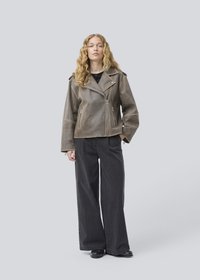 Brown leather biker jacket with a zipped front, wide lapels, and angled pockets, worn over a black top and paired with wide black trousers.