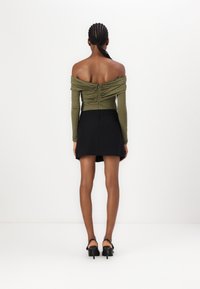 Bluzka w kolorze oliwkowym, odsłaniająca ramiona, z marszczeniami, zestawiona z czarną mini spódnicą. Modelka nosi czarne sandały na obcasie z odkrytymi palcami.