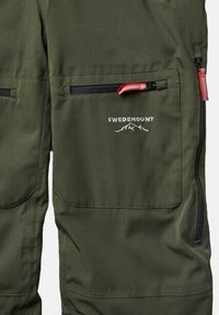 Gröna vattentäta byxor med dragkedjefickor, utrustade med röd dragkedjesläppare och "SWEDEMOUNT"-logotyp broderad ovanför bergsgrafik.