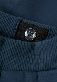Marineblauwe stof met een ribbelstructuur, voorzien van een gladde ronde zilveren knop met een ontwerp van vier gaten en een zwarte elastische band eronder.