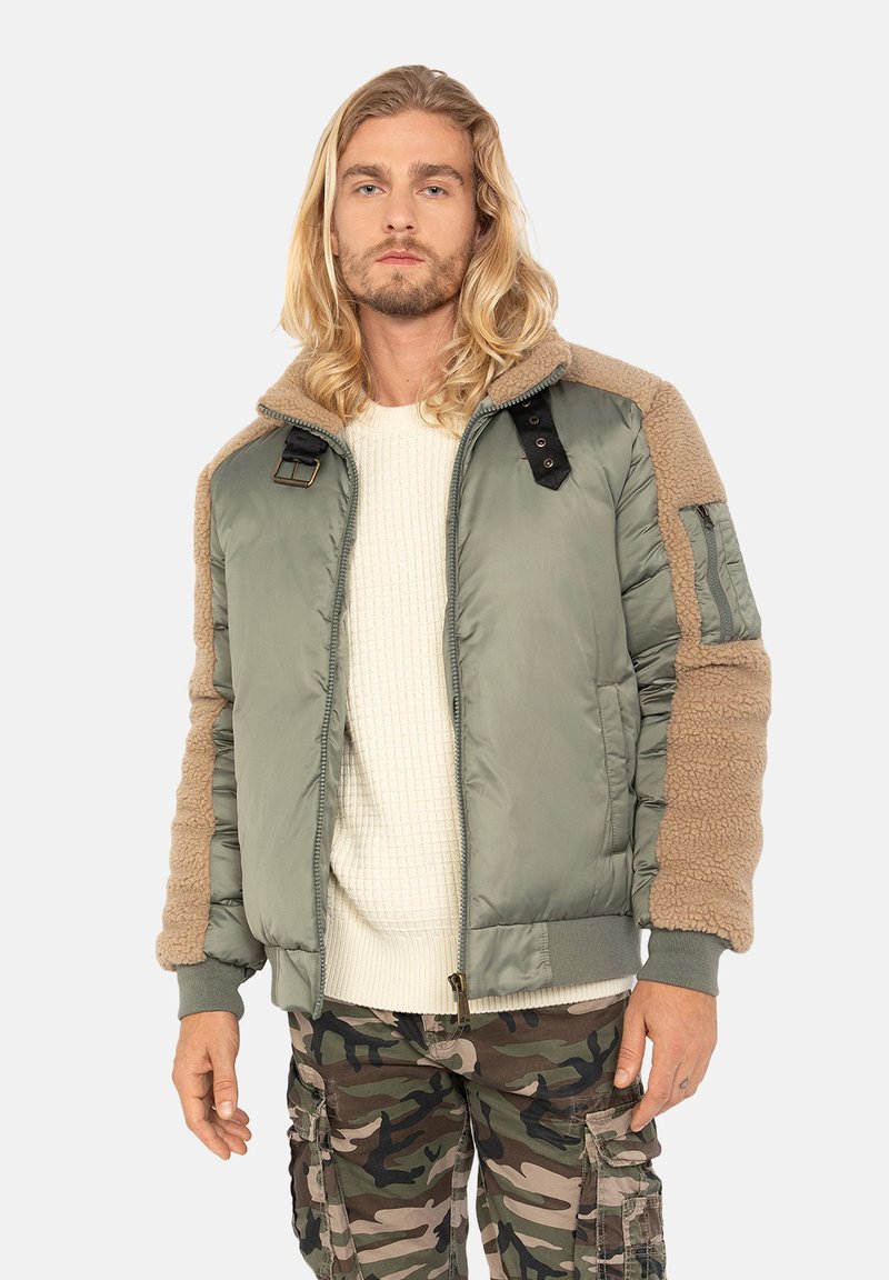 Grøn bomberjakke med beige fleece-detaljer, lynlås foran og ribbede manchetter, parret med en cremet sweater og camouflage cargo-bukser.