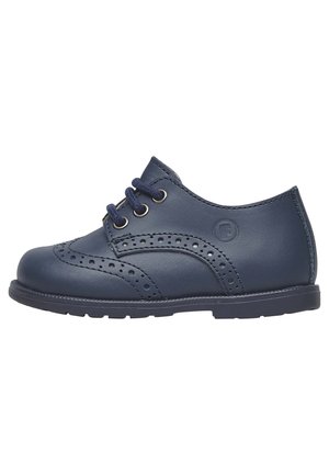Chaussure brogue enfant en cuir bleu marine avec perforations en ailes, trois œillets avec lacets bleu marine et semelle en caoutchouc.