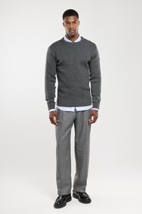 Pull gris foncé avec tricot texturé, col rond et boutons sur les épaules, sur une chemise à col bleu clair ; associé à un pantalon en tartan gris clair et des chaussures noires.