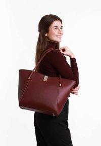 Bordová taška přes rameno vyrobená z hladké kůže, s pozlacenými prvky, širokými popruhy a zúženým designem s logem na přední straně.