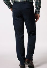 Marinblå byxor i slätt tyg, med två bakfickor som har knappar. Försedda med raka ben och matchade med bruna läderskor.