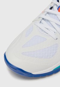 White athletic shoe with mesh and synthetic materials, featuring a textured surface, blue outsole, and multicolored accents near the laces.