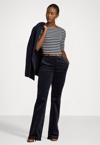 Tumedat säärelahkstega corduroy püksid tekstureeritud viimistlusega, koos sobiva valge ja tumesinine triibuline topp ja vastava bleiseriga, millel on pruun vööp.