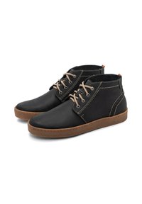 Stivali alla caviglia in pelle nera con lacci marroni, cuciture a contrasto e suola in gomma marrone. Punta rotonda, design a metà-tallone con accenti minimi.