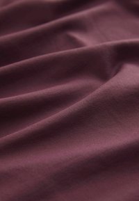 Bordeaux-stof med en glat tekstur, der har naturlige folder og subtil stræk. Overfladen fremstår blød og let reflekterende.