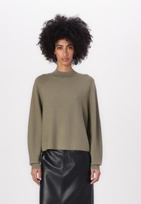 Olive green knitted sweater with a high neckline, dropped shoulders, and long sleeves, paired with a black leather skirt. Soft texture.