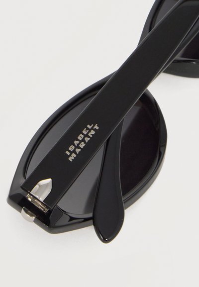 Μαύρα υπερμεγέθη γυαλιά ηλίου με οβάλ φακούς και την επιγραφή «ISABEL MARANT» στο μπράτσο σε χρυσά γράμματα, σε λευκό φόντο.