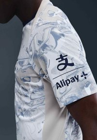Camiseta gráfica con una tela de color claro y estampado con acentos azules, que exhibe el logotipo de "Alipay" en la manga.