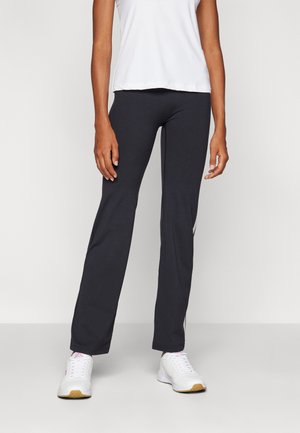 Black activewear pants with a slim fit, made of stretchy material, featuring a contrasting white stripe along the side, paired with white sneakers.