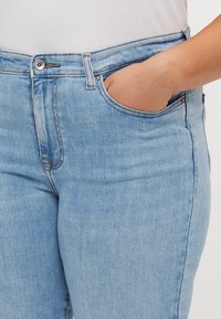 Gai zili džinsi ar augstu jostasvietu, ar vara pogu aizdari, divām priekšējām kabatām un gludu, teksturētu apdari.