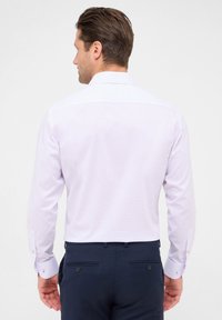 Lichtpaarse overhemmed die een klein ruitpatroon heeft, met lange mouwen en een klassieke kraag. Draagt het met donkerblauwe broek.