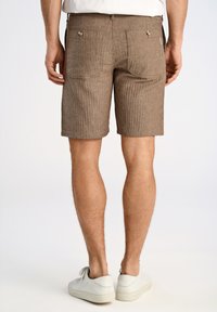 Pantalones cortos a rayas marrones hechos de tela texturizada, con dos bolsillos traseros con botones y un ajuste de altura media. Llevados con zapatillas blancas.