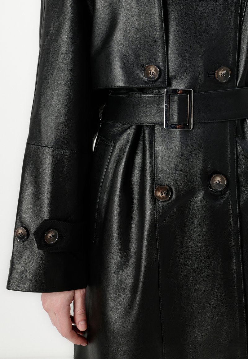 Schwarzer Ledermantel mit einem doppeltknöpfigen Design, braunen Knöpfen, tailliertem Schnitt und glatter Textur.