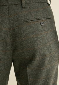 Pantalons en laine vert foncé avec une texture douce. Présente un motif à carreaux marron, une poche plate à l'avant et un détail de bouton noir unique.