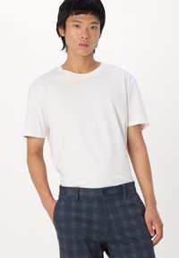 Camiseta de algodón blanca de manga corta, con escote redondo, combinada con pantalones a cuadros azules que tienen un cierre de botón y dos bolsillos.