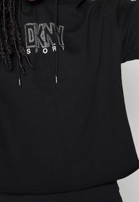 Svartkortad sweatshirt i mjukt material med huva och en "DKNY SPORT"-logotyp prydd med kristaller på framsidan.