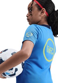 Maillot de sport bleu à manches courtes, arborant le logo jaune "THFC" et l'emblème Nike. Un ballon de football blanc est tenu sous le bras.