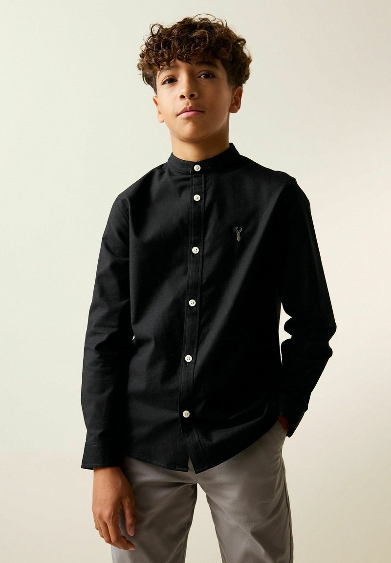 Camicia nera con bottoni, collo alla coreana, bottoni bianchi e un piccolo ricamo sul petto. Tessuto dalla texture liscia.