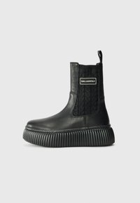 Bottes chelsea en cuir noir avec une semelle striée et un panneau élastique texturé portant un logo sur le côté. Finition lisse, design moderne.