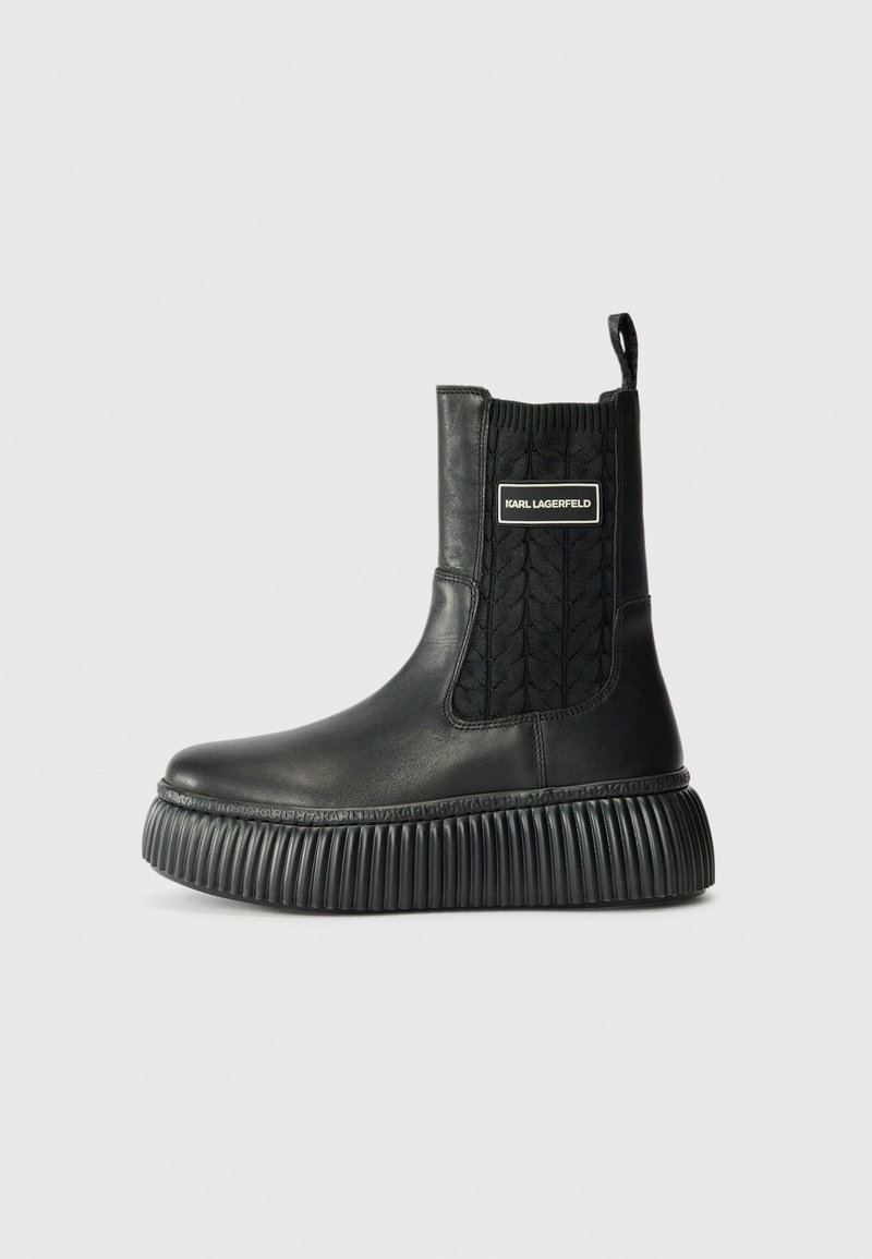 Bottes chelsea en cuir noir avec une semelle striée et un panneau élastique texturé portant un logo sur le côté. Finition lisse, design moderne.