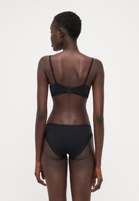 Ensemble de lingerie noire comprenant un soutien-gorge et un bas avec des accents en dentelle. Tissu doux avec des bretelles réglables et une fermeture à crochets à l'arrière.