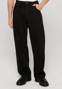 Mustad mustadest puuvillast laiad püksid, millel on sile tekstuur, nupuga kinni keeratavad ja tavalised taskud.