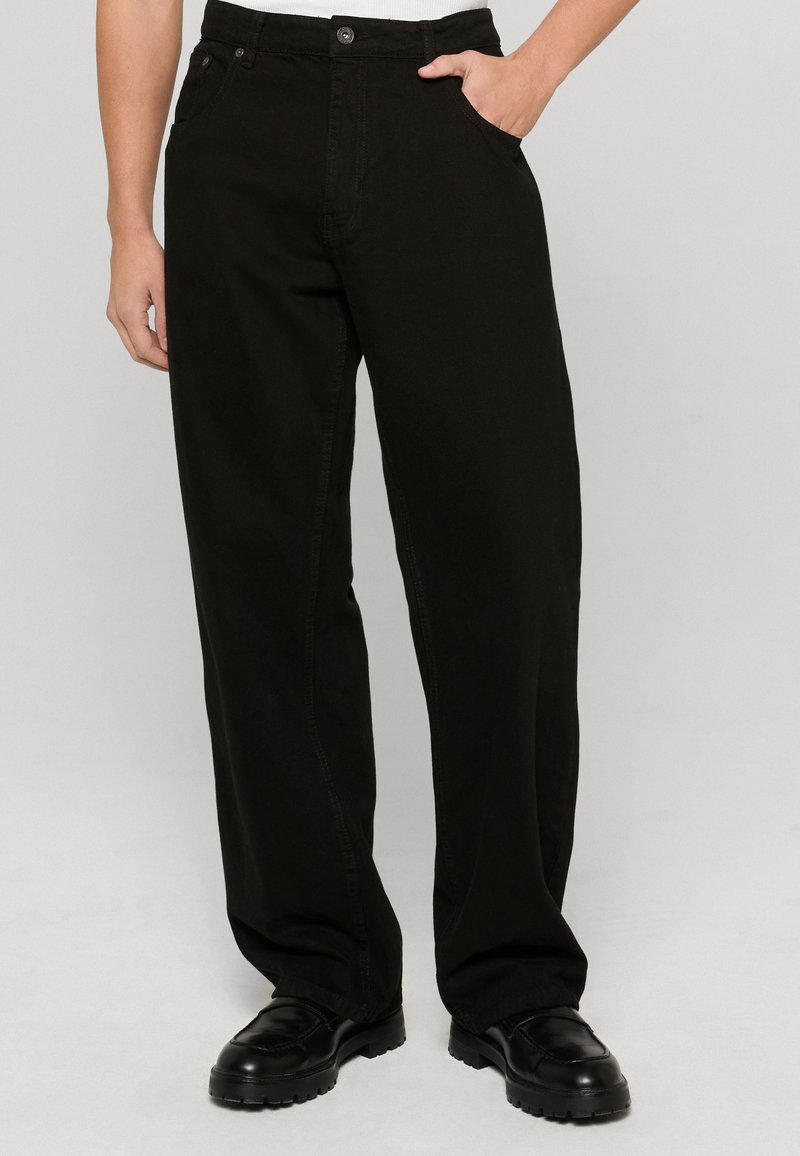 Mustad mustadest puuvillast laiad püksid, millel on sile tekstuur, nupuga kinni keeratavad ja tavalised taskud.