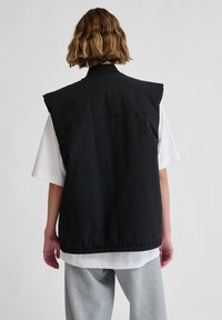 Schwarze ärmellose Weste mit hohem Kragen, aus glattem Stoff. Verfügt über einen lockeren Schnitt, elastischen Saum und ein einfaches Design ohne Muster.