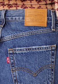 Niebieskie dżinsy z pomarańczowym przeszyciem, skórzana metka z napisem "Levi Strauss & Co." na pasku, oraz charakterystyczna czerwona metka na tylnej kieszeni.
