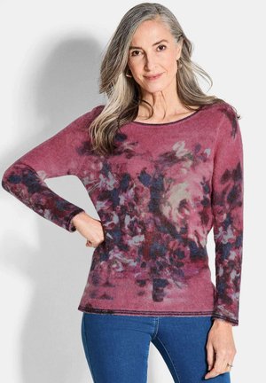 Maglione a maniche lunghe nei toni del rosa e del viola con motivi floreali, textura morbida e scollatura rotonda, abbinato a jeans blu.